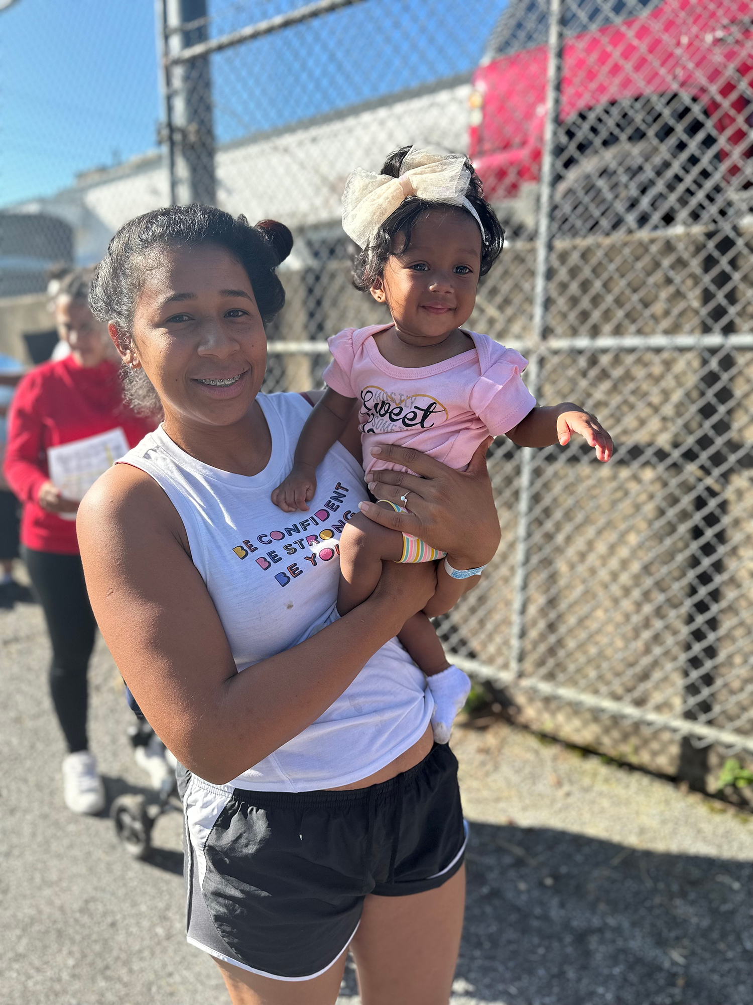 Smiling woman holds baby outdoors.